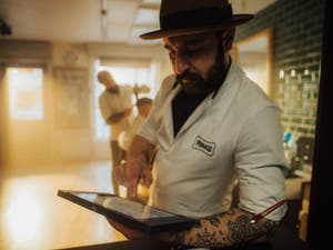 Tattooed man in a fedora checking his PayPal Point of Sale in a barbershop