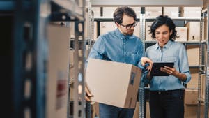 Two supply chain employees in a warehouse looking at a tablet.