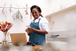 A woman in her small business shop looking at her phone and exploring small business grants in the United Kingdom.