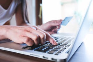 woman holding credit card while typing on laptop