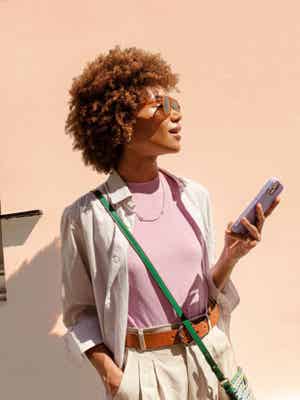 Frau steht draußen in der Sonne und hält ihr Handy