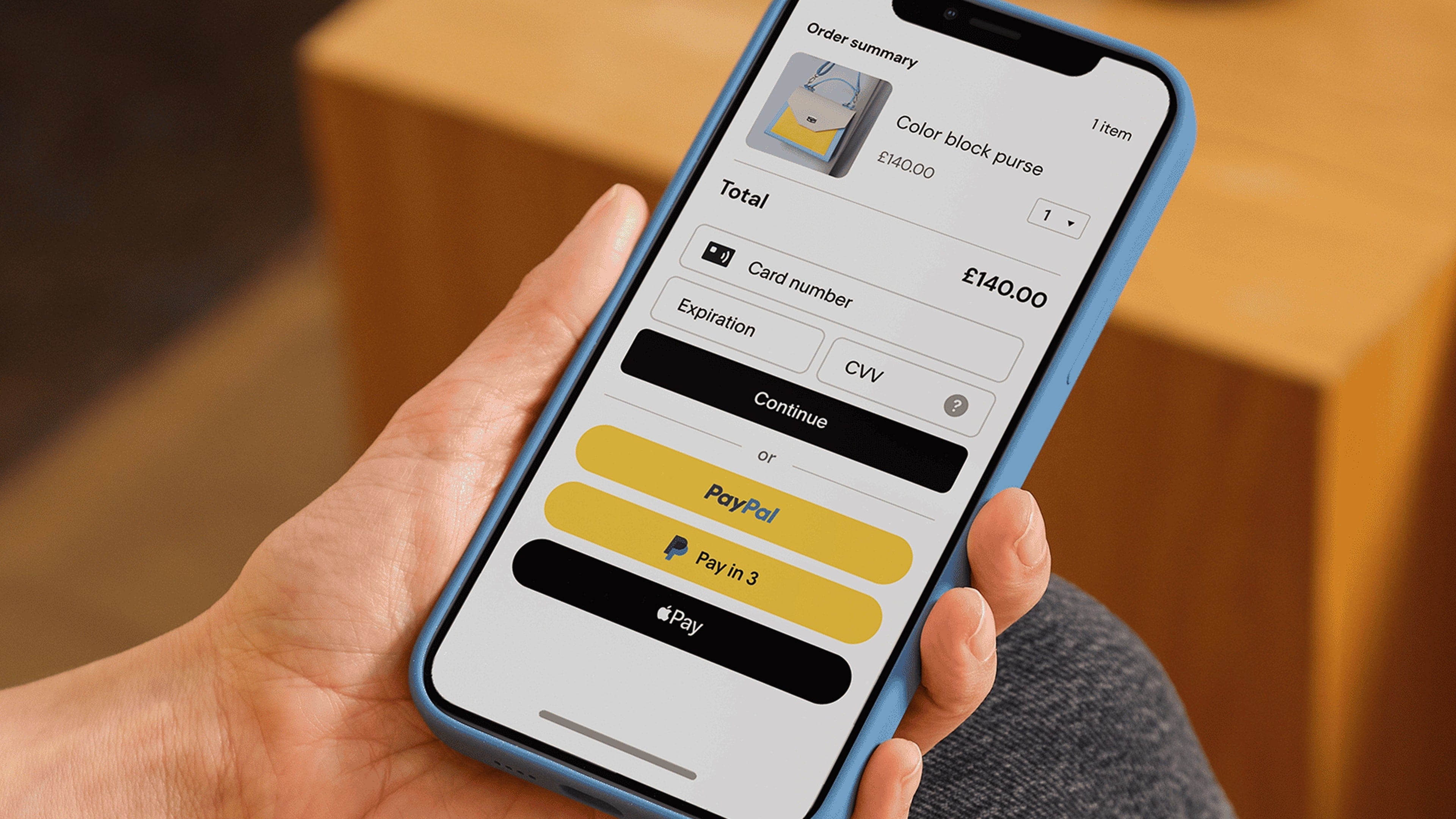 Person holding mobile phone showing checkout screen with payment options including debit/credit card, PayPal, Pay Later, and Apple Pay